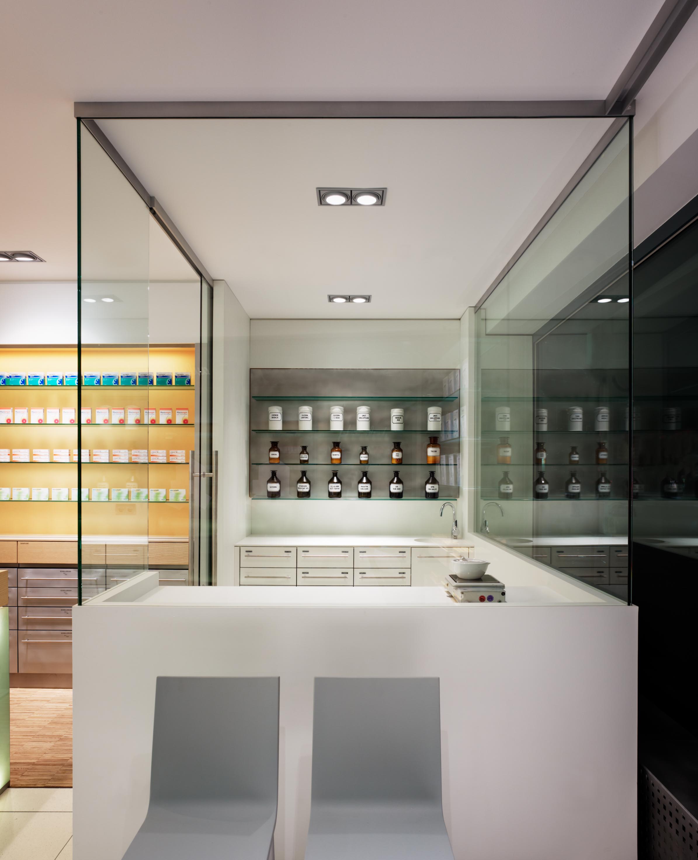 Frontalansicht der minimalistisch eingerichteten, raumhoch verglasten Rezeptur mit weißen Corian-Arbeitsflächen