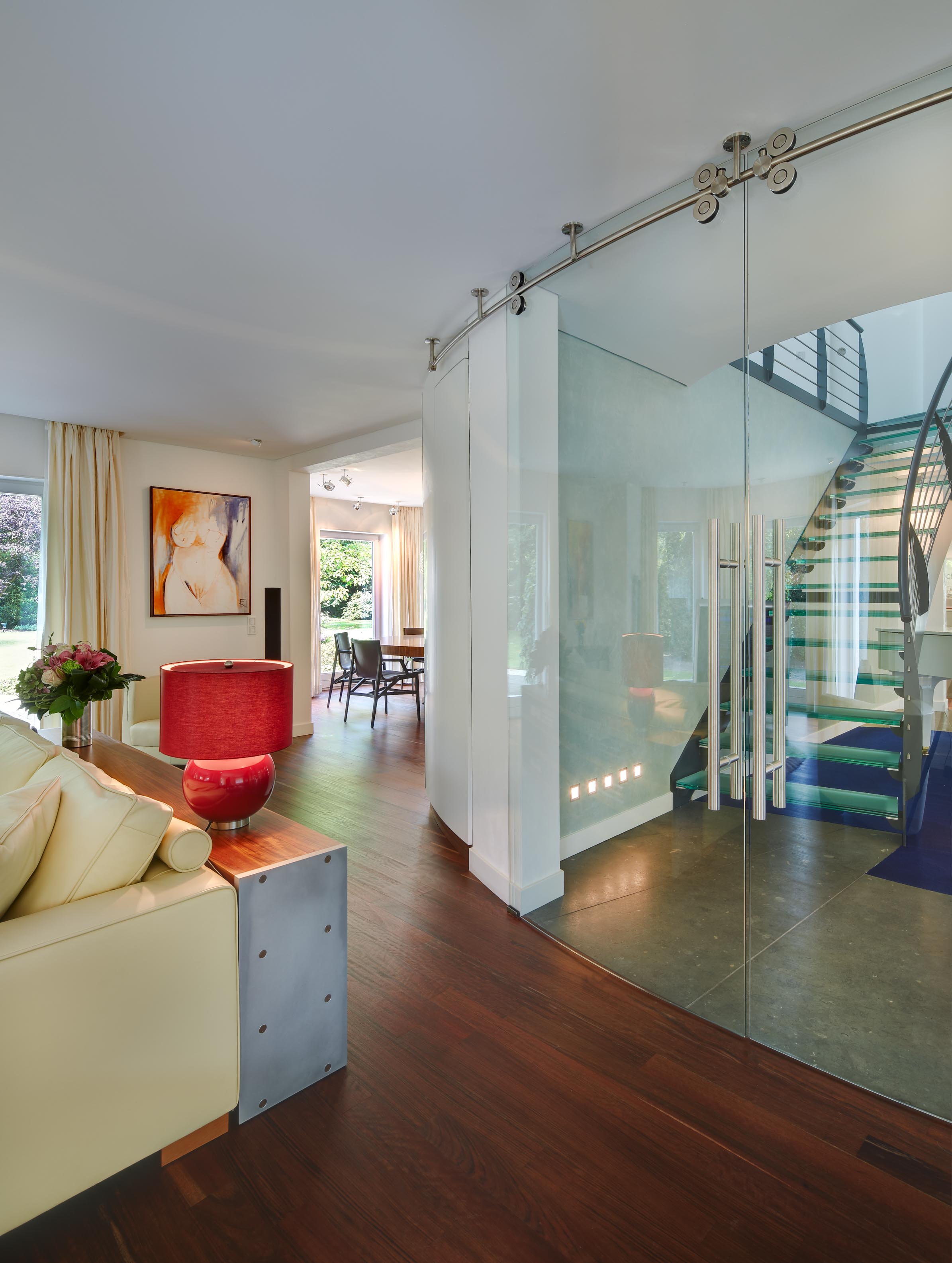 Wohnzimmer mit Blick durch die gebogene Ganzglastür ins Entrée